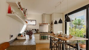 A modern kitchen with white cabinets, a wooden island, and a large window offering a view of greenery. - Paris Mimosa Penthouse Residences (Boulogne-Billancourt)