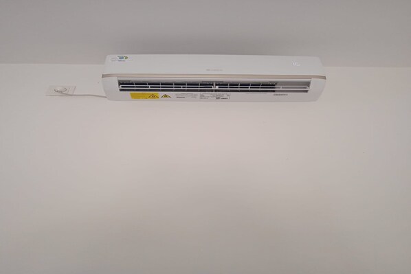 Een witte, aan de muur bevestigde airconditioner met bedieningspaneel en een waarschuwingsticker.