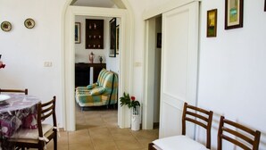 A dining area with a table and chairs, a sofa in the background, and a doorway leading to another room. - Villa with private pool and garden (Marina di Grosseto)