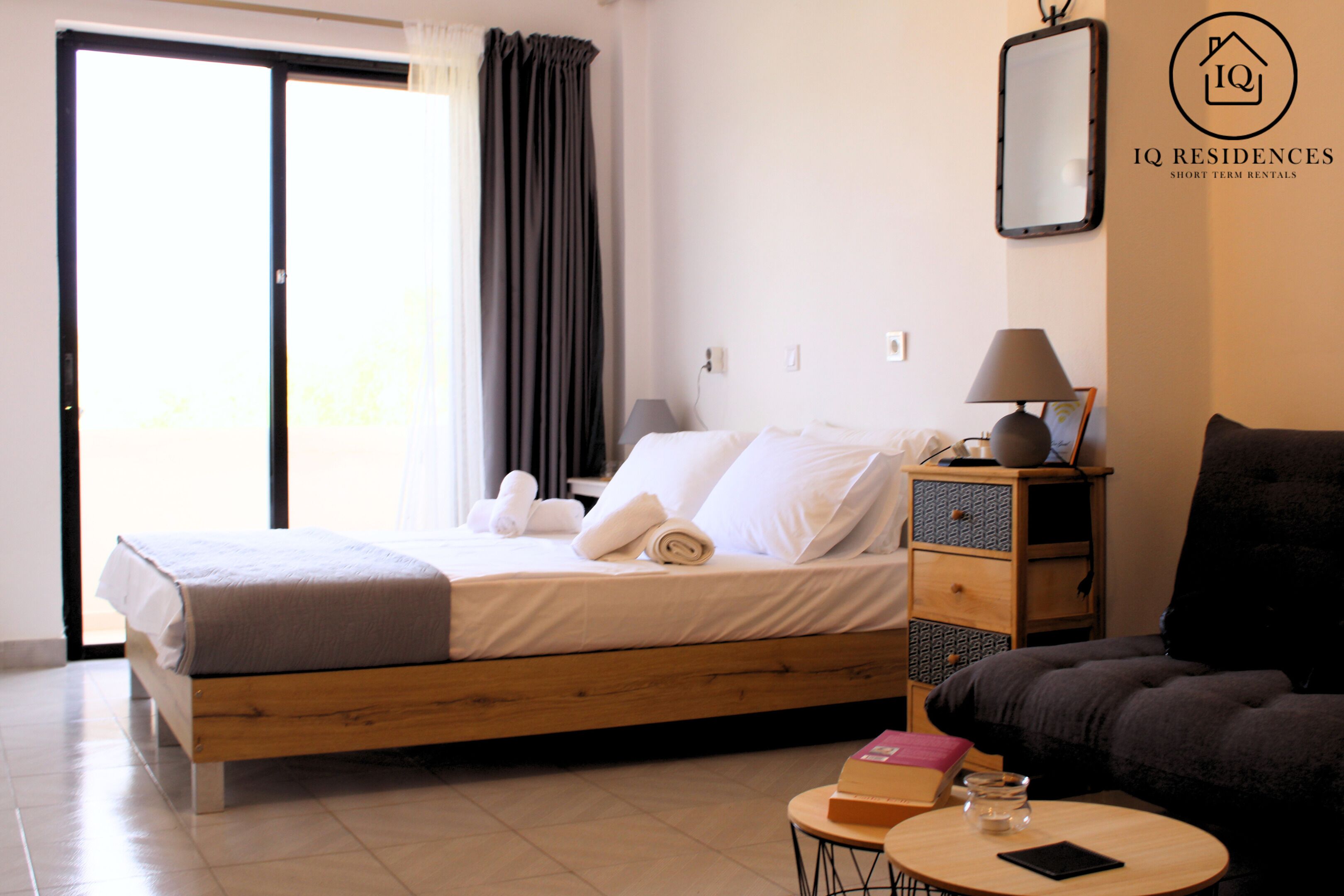 A bedroom with a bed, a bedside table with a lamp, a sofa, and a small round table with a book and a glass.