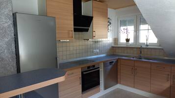 A modern kitchen with a built-in dishwasher, a stainless steel refrigerator, wooden cabinets, and a window with a view of the outdoors.