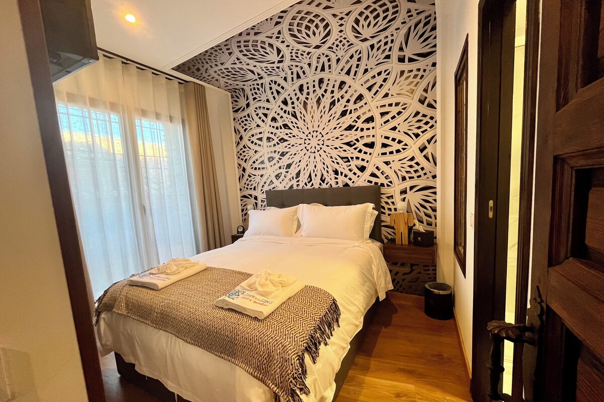 A hotel room with a bed, a decorative wall, a nightstand, and a door.