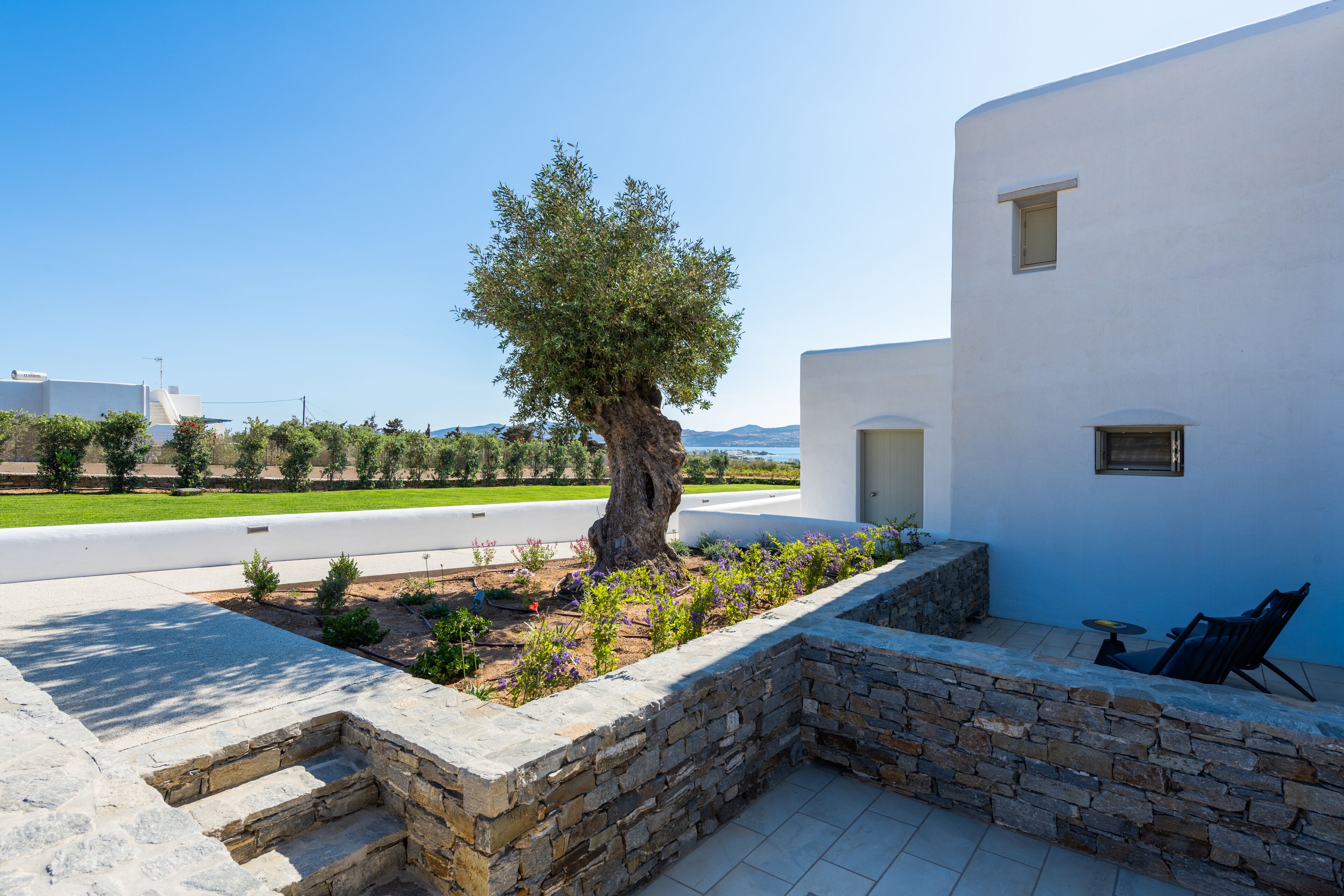 A modern building with a stone retaining wall, a tree, and a patio area with outdoor furniture.