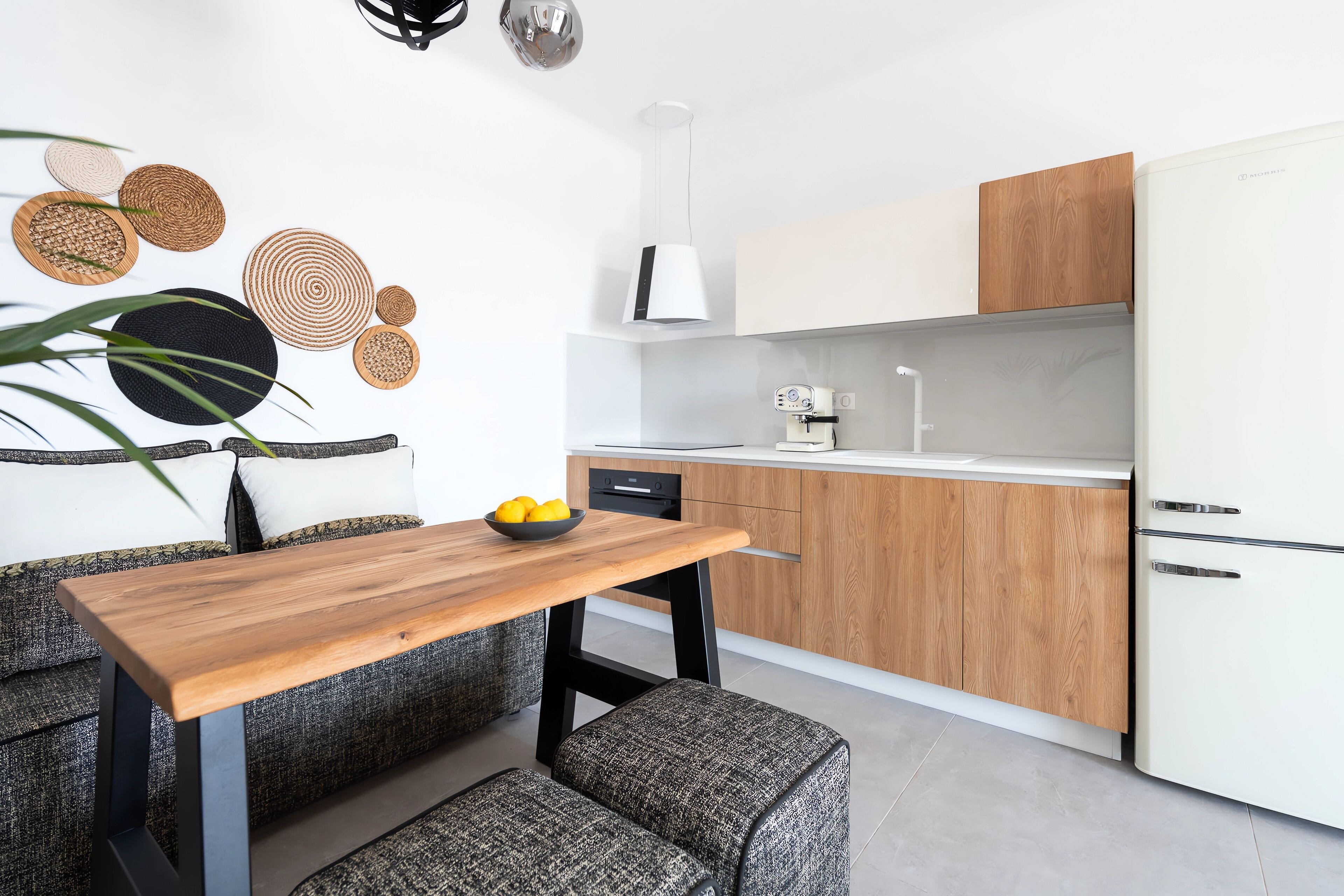 Une cuisine moderne avec une table en bois, un banc recouvert d’un tissu gris et un réfrigérateur blanc.