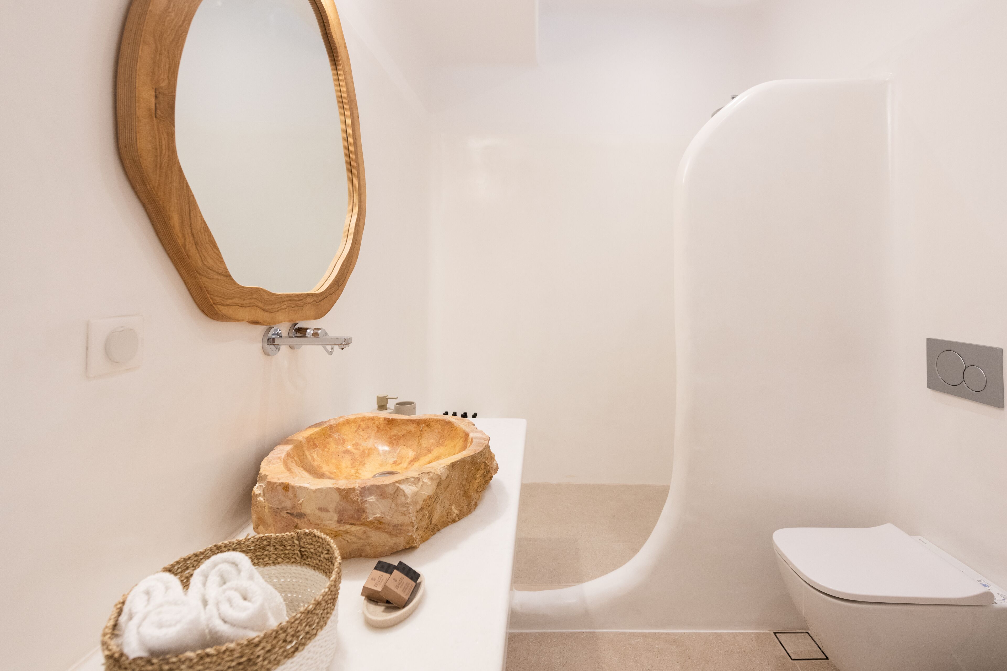Un baño con un lavabo de piedra, un espejo con marco de madera, un inodoro blanco y un cesto para toallas.