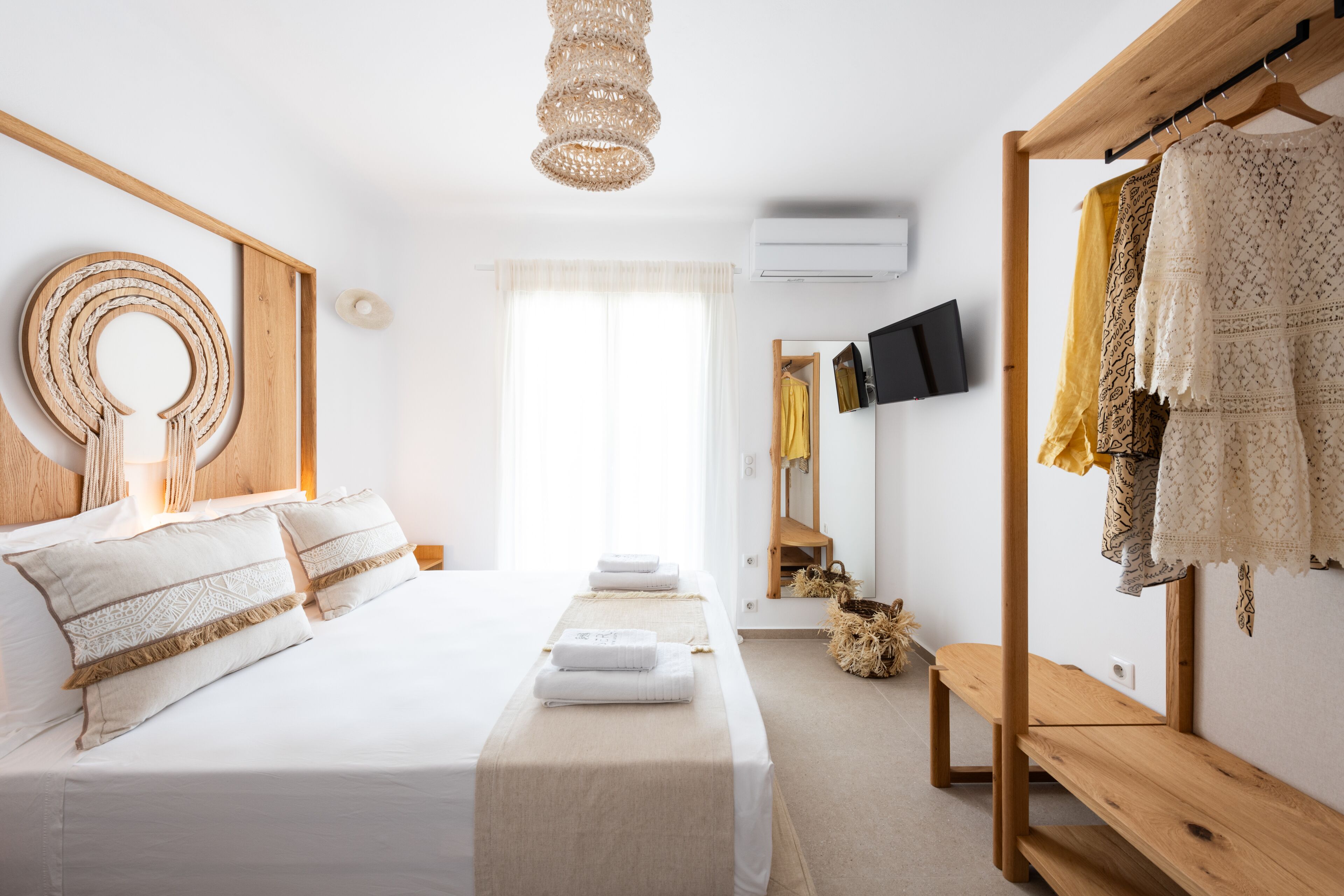 A bedroom with a bed, bedside tables, a wooden bench, a hanging light fixture, a wardrobe, and a television.