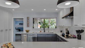 Cocina moderna con armarios blancos, una ventana con vistas a la vegetación y un horno empotrado.