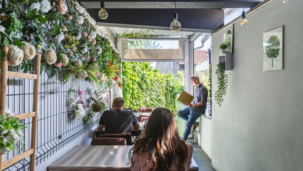 A restaurant with a long counter, wooden chairs, and a wall adorned with plants and flowers. - Hostel e Cia Porto (Porto)