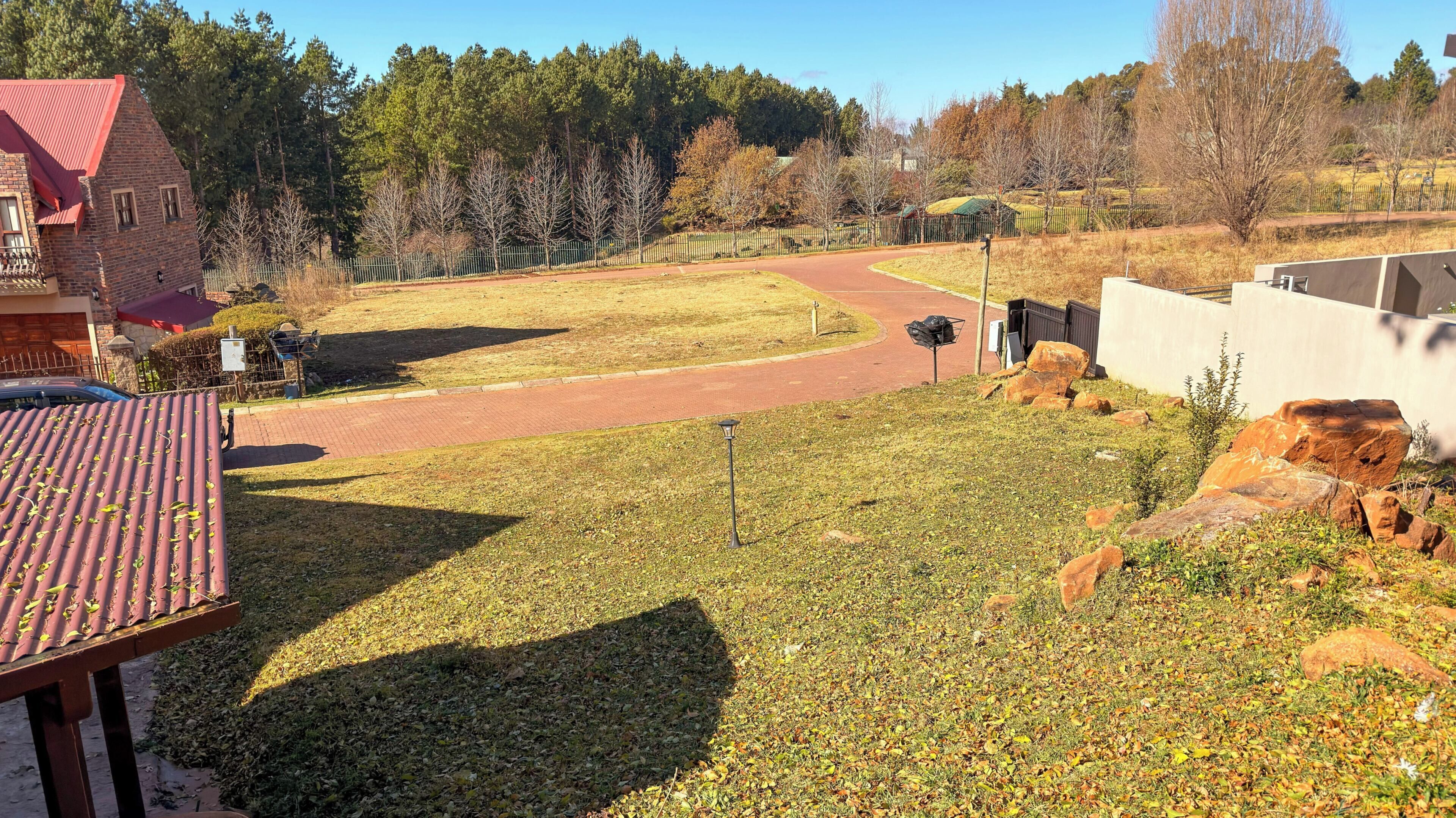 A paved path, a building with a red roof, and a fenced area with trees and rocks.