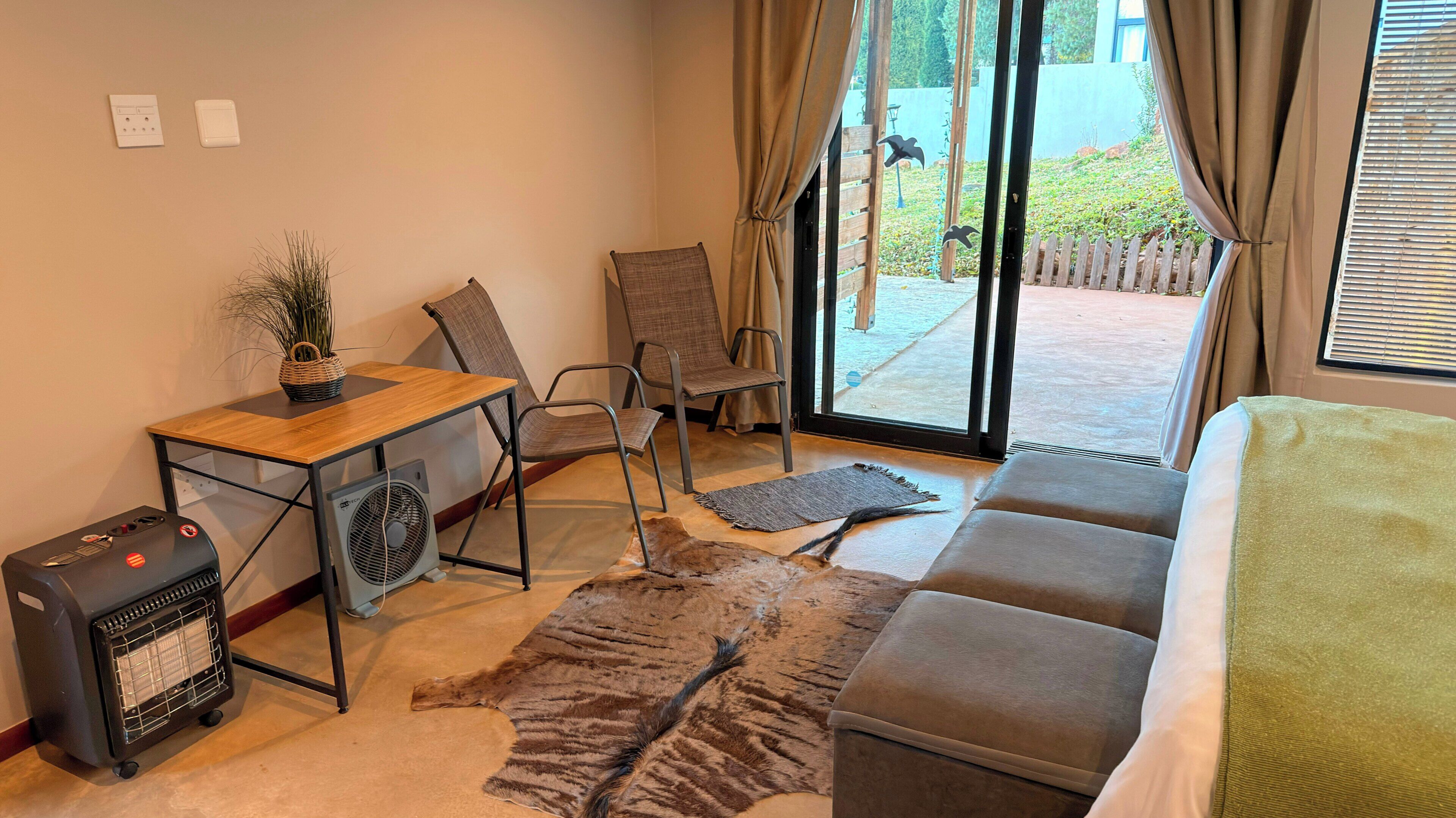 Una habitación con un sofá, una mesa con un ventilador, una silla, un tapete y un calentador.