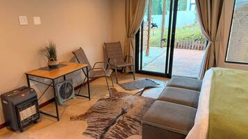 Una habitación con un sofá, una mesa con un ventilador, una silla, un tapete y un calentador.