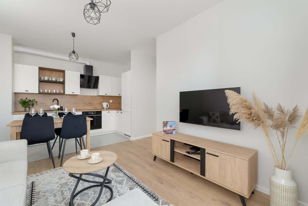 A modern living room with a dining area, a TV mounted on the wall, and a wooden cabinet.