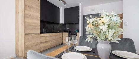 A modern dining area with a wooden cabinet, a dining table set with plates, glasses, and a vase with flowers.