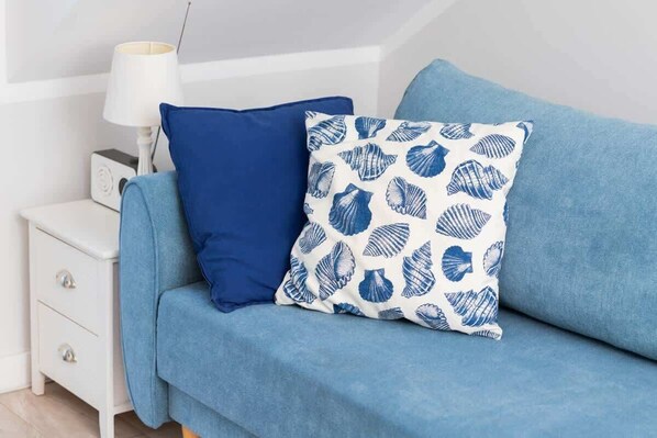 A blue sofa with two pillows, one solid blue and one with a shell pattern, against a white wall.