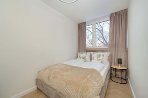 Quarto com cama, mesa de cabeceira e janela com cortinas.