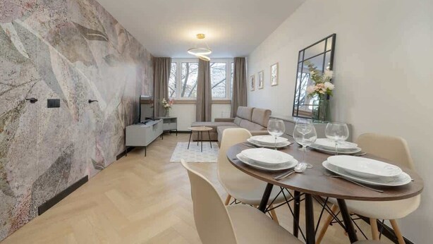 Un comedor moderno con pared de mármol, una mesa de comedor con platos y vasos, y un sofá al fondo.