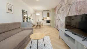 Una sala de estar moderna con un sofá, una mesa de centro, un televisor de pantalla plana y una cocina al fondo.