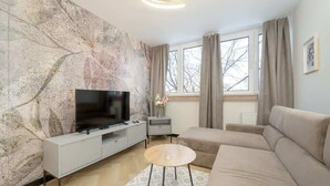 Una sala de estar moderna con un televisor de pantalla plana, un sofá, una mesa de centro y un gran ventanal con cortinas.