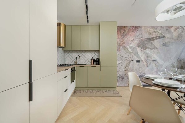 A modern kitchen with light green cabinets, a marble backsplash, and a dining area with a table set for two.