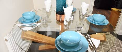 A round glass table set with blue bowls, plates, and clear glasses, accompanied by white napkins and cutlery.