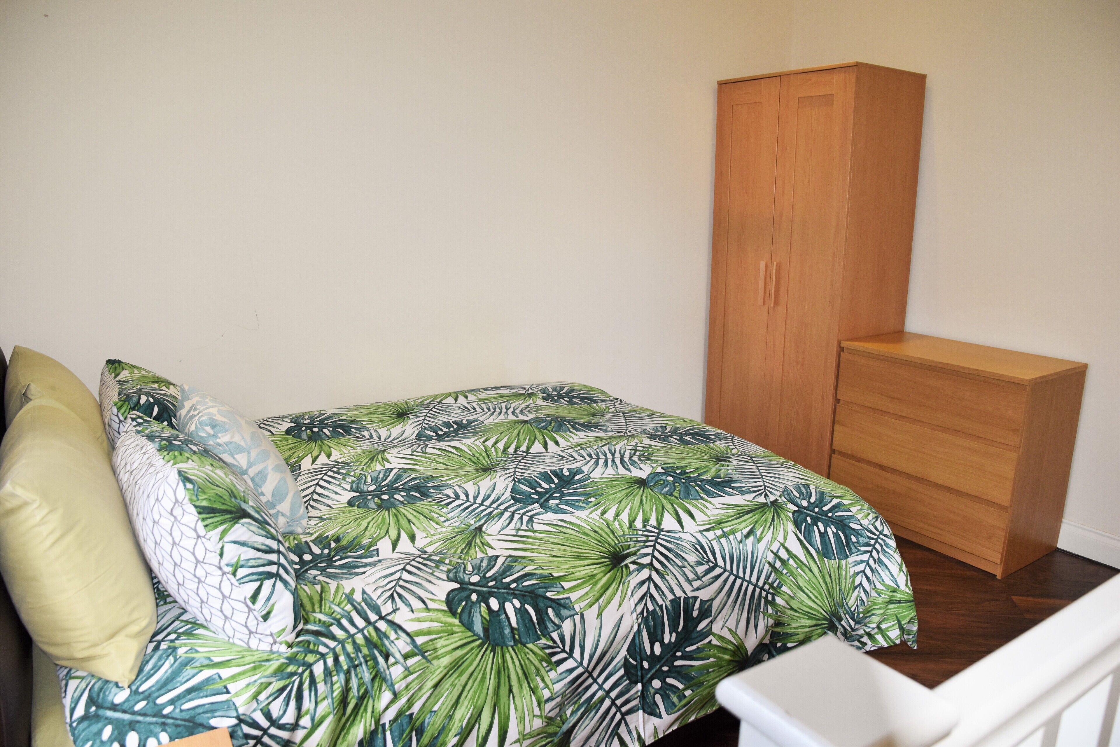 Een slaapkamer met een bed, een houten garderobe en een witte nachtkastje.