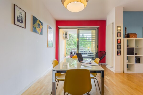 Una sala de estar moderna con una mesa de vidrio, sillas amarillas, una pared de acento roja y vista a zonas verdes al exterior.