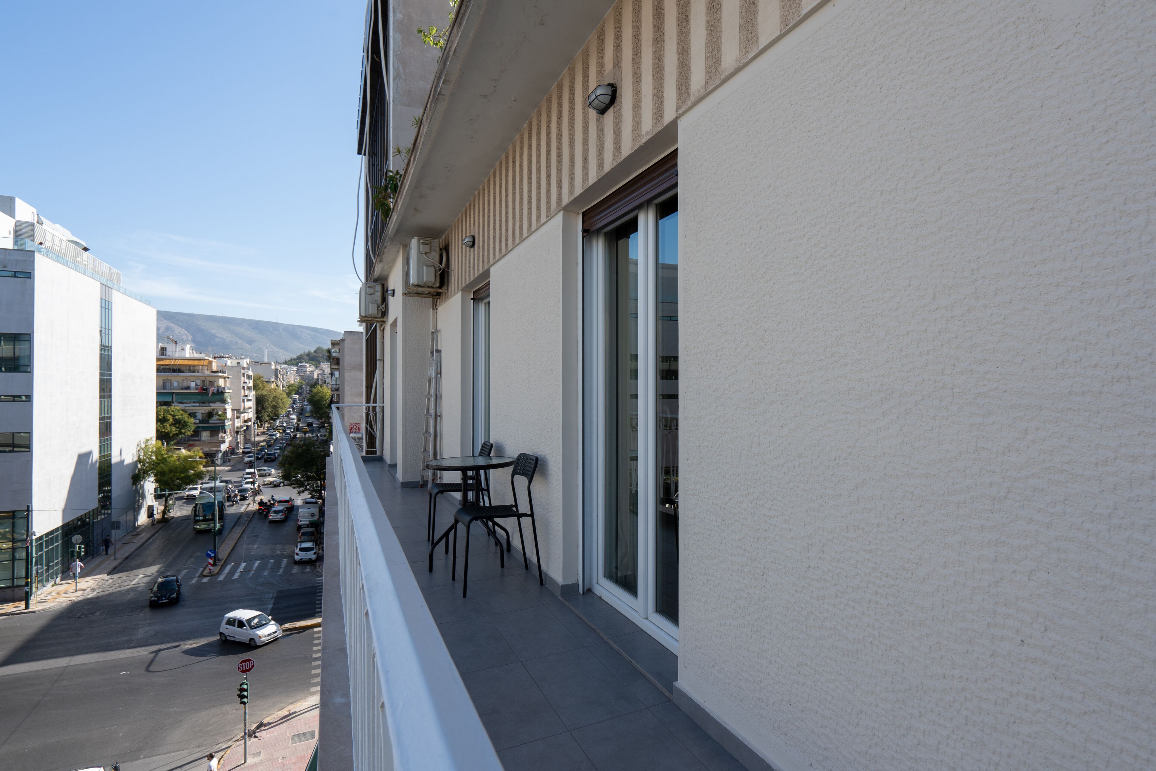 A balcony with a table and chairs, overlooking a city street with cars and buildings.