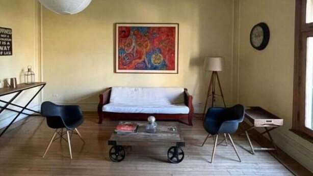 Una sala de estar con un sofá, dos sillones, una mesa de centro, un cuadro, una lámpara y un reloj en la pared.