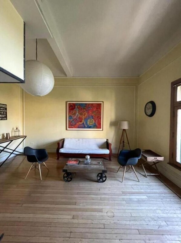 Uma sala de estar com sofá, duas cadeiras, mesa de centro, um quadro, abajur e relógio na parede.