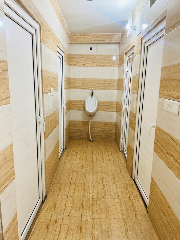 A narrow hallway with a urinal in the center, flanked by two doors on either side. - Hotel M K Grand (Varanasi)