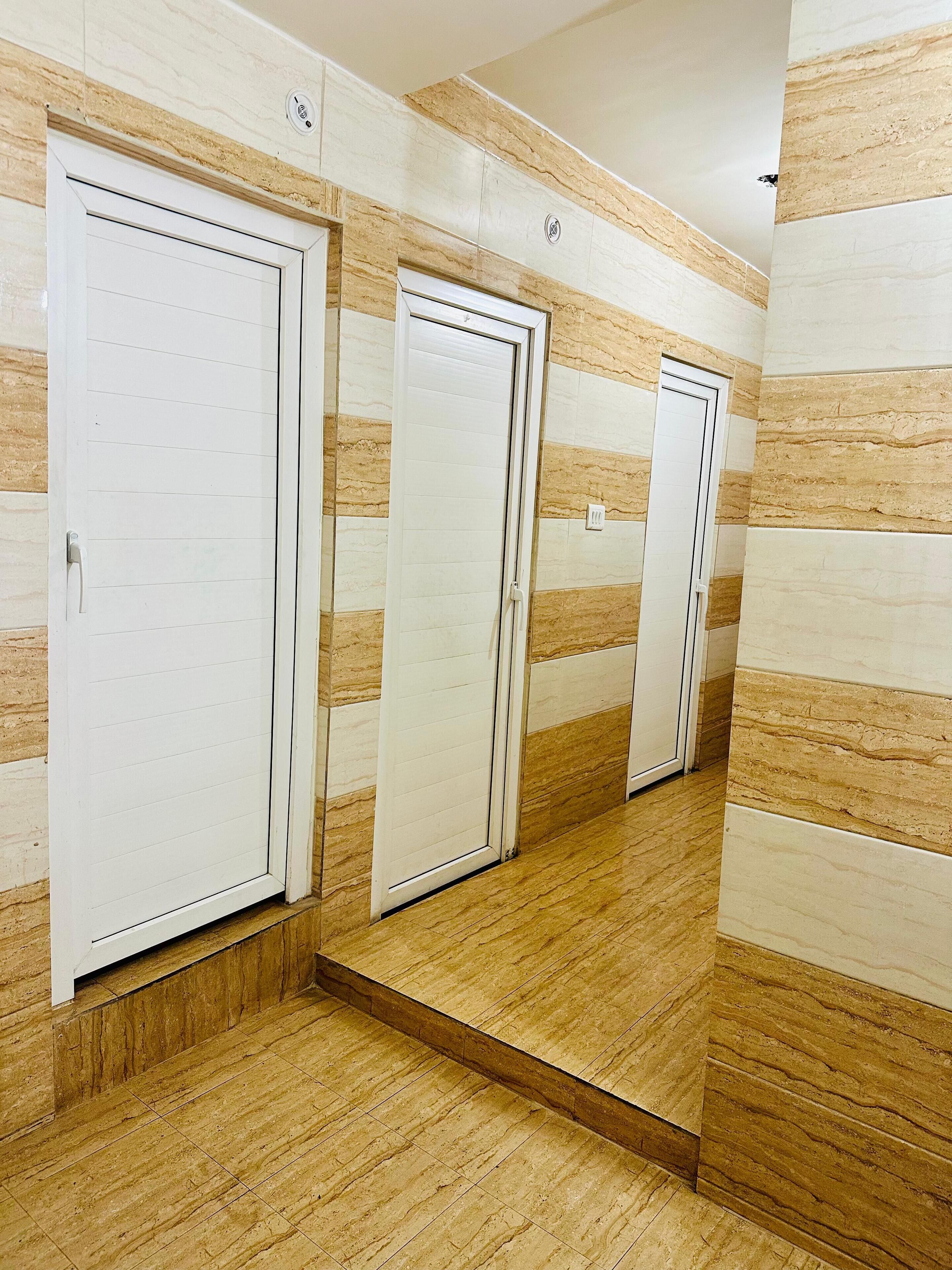 Un pasillo con tres puertas blancas, cada una con pomo, en una pared con un diseño parecido al mármol. El suelo está cubierto de baldosas con un patrón similar.