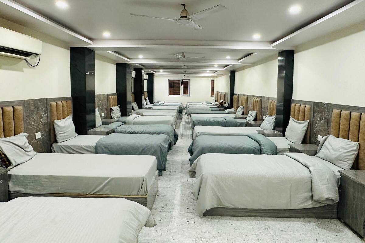 Habitación de hotel con varias camas dispuestas en filas, unidades de aire acondicionado, ventiladores de techo y piso de mármol.