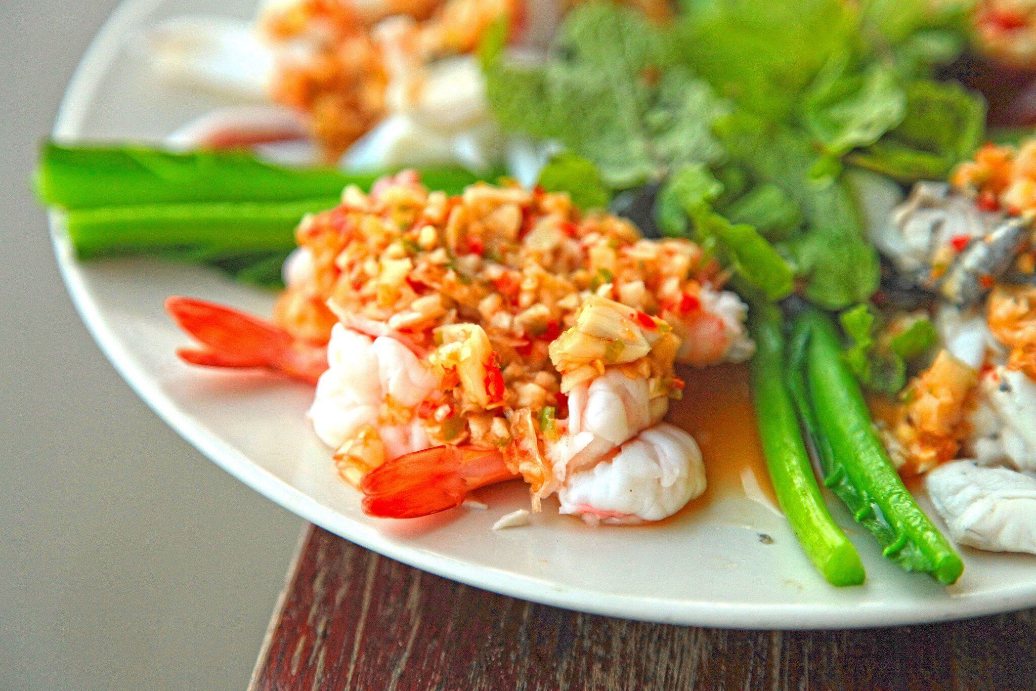 Un plato de comida con camarones, verduras verdes y salsa.