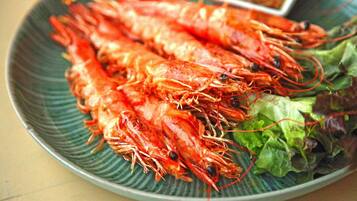 Un plato de camarones cocidos, acompañado de verduras y un recipiente pequeño con salsa.