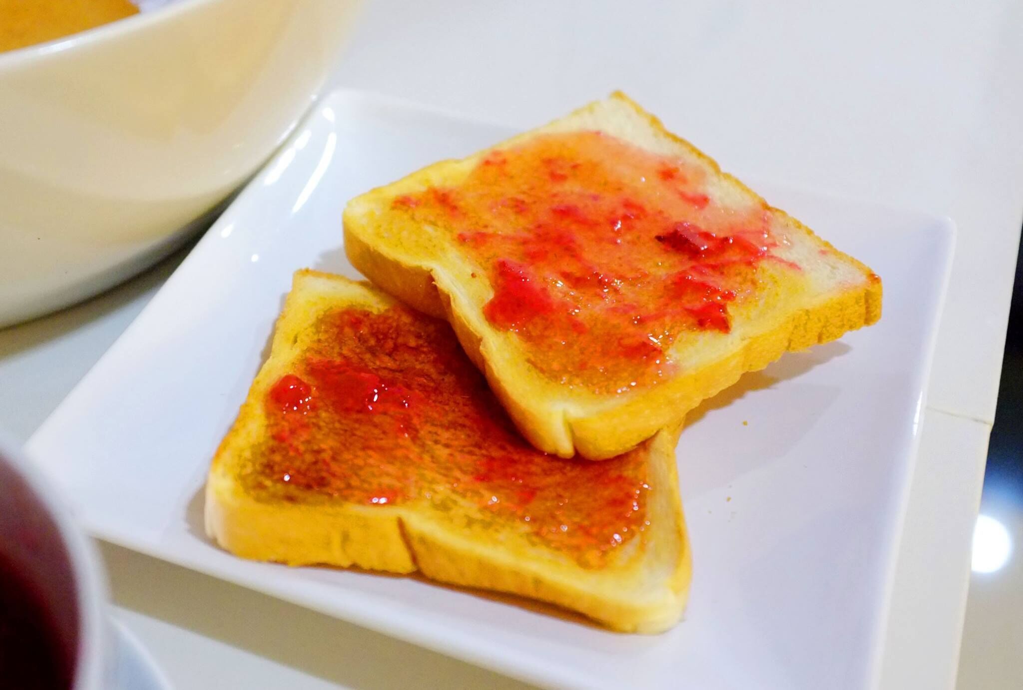 Two slices of toast with jam on a white plate.