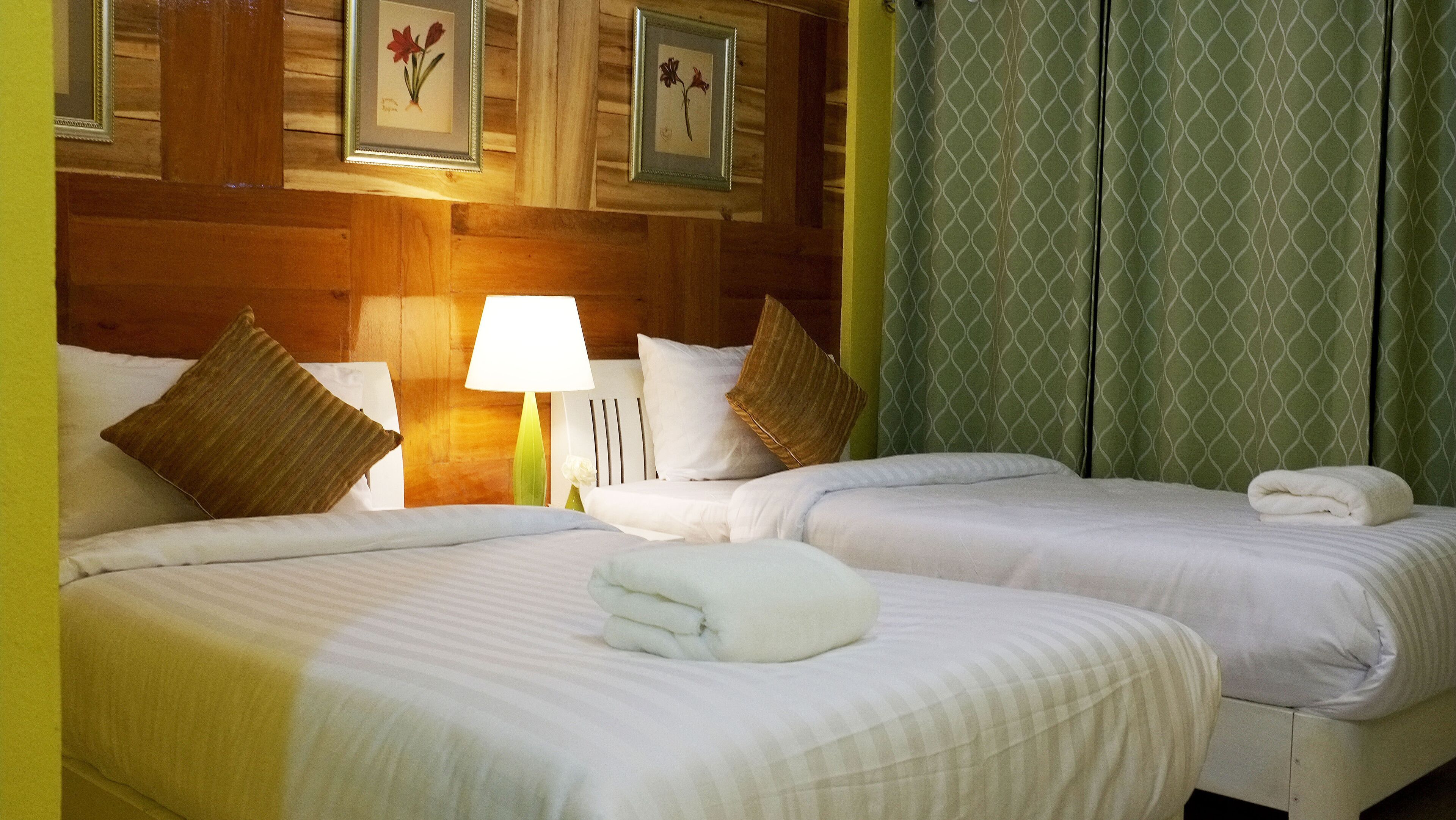Habitación de hotel con dos camas, una mesita de noche con lámpara e impresión botánica enmarcada en la pared.