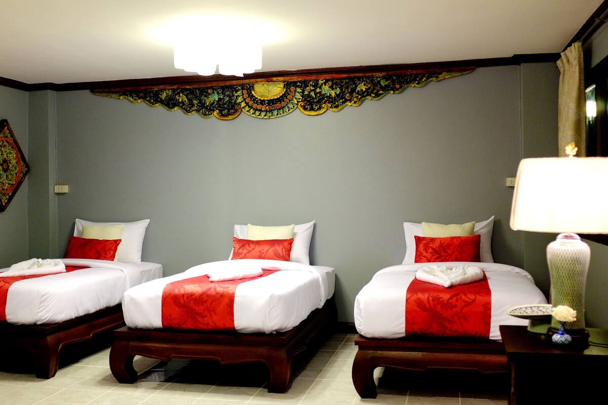 A hotel room with three single beds, each with a red and white bedspread, and a decorative wall hanging above the beds.