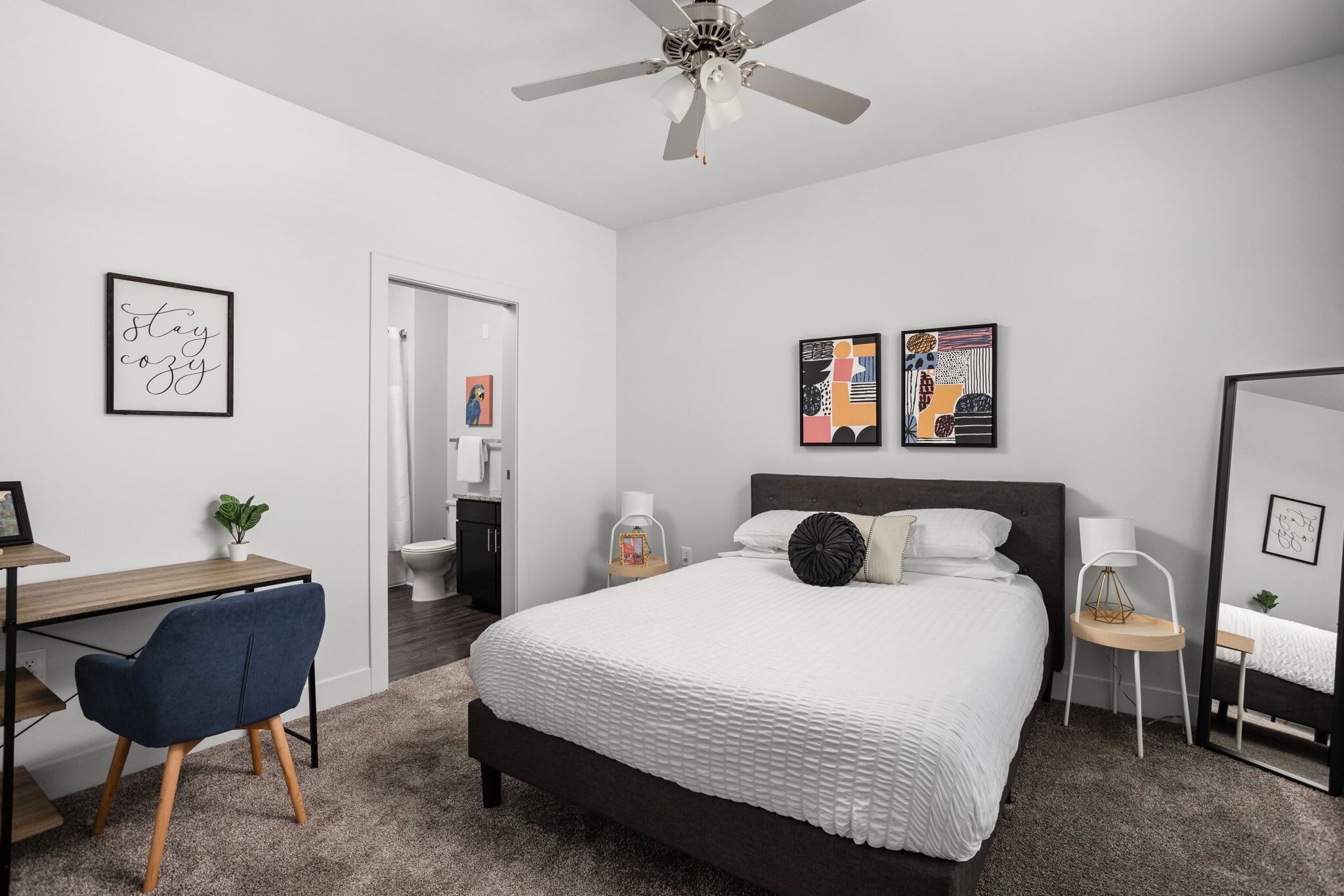 A modern bedroom with a bed, desk, chair, and a ceiling fan.