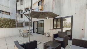 An outdoor patio with wicker furniture, a table, and a large umbrella. - Pateo IN Lapa City Center by Vacationy (Porto)