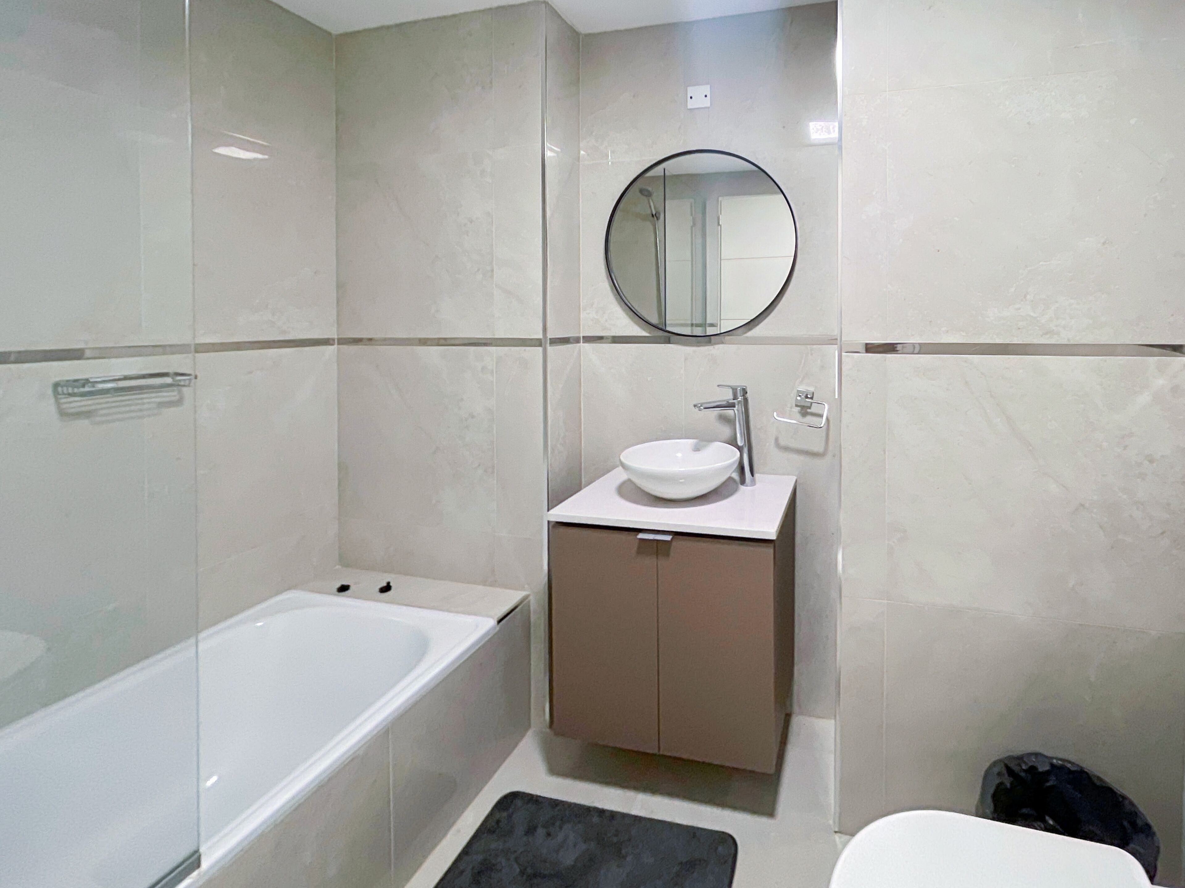 Ein modernes Badezimmer mit einer Badewanne, einem runden Spiegel und einem Waschbecken mit Schrank.