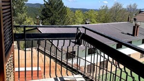 A balcony with a metal railing overlooking a courtyard with a tiled floor and a view of a forested area and distant hills. - 2 Bedroom Apartment in Celico (Celico)