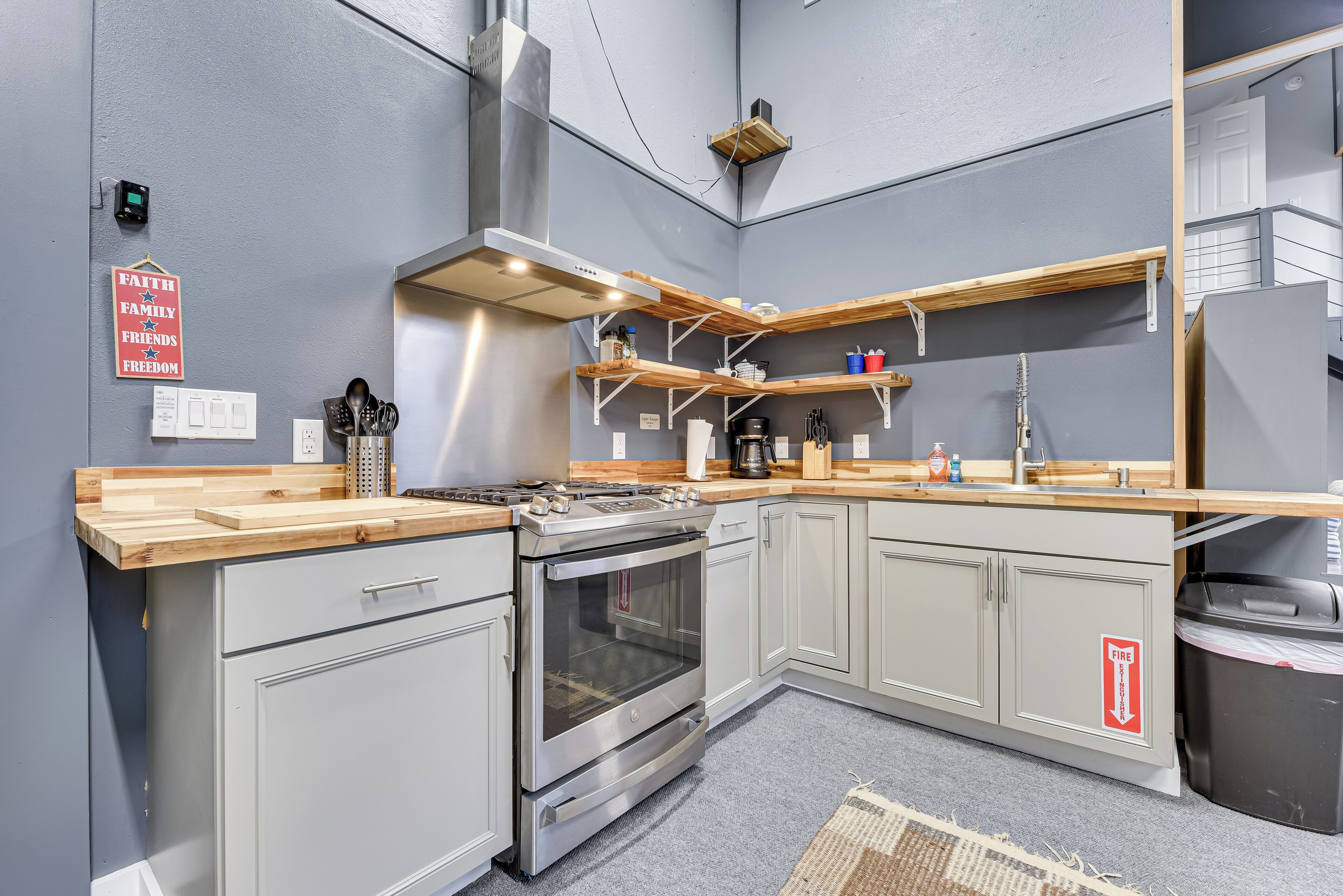 A modern kitchen with grey cabinetry, stainless steel appliances, wooden countertops, and built-in shelves.
