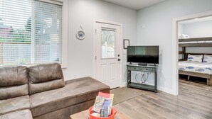 A living room with a brown sofa, a TV on a stand, a bookshelf, and a bed with a bunk. - Westport Home w/ Hot Tub: 2 Blocks to Beach! (Westport)