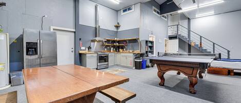 Una habitación amplia con una mesa de madera, mesa de billar, kitchenette y una escalera.