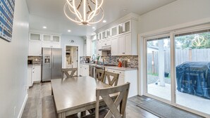 A modern kitchen with white cabinets, a large dining table, and a chandelier. - Westport Home w/ Hot Tub: 2 Blocks to Beach! (Westport)