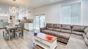 A modern kitchen with white cabinets, a dining area with a wooden table and chairs, and a brown leather sofa in a living room with large windows. - Westport Home w/ Hot Tub: 2 Blocks to Beach! (Westport)