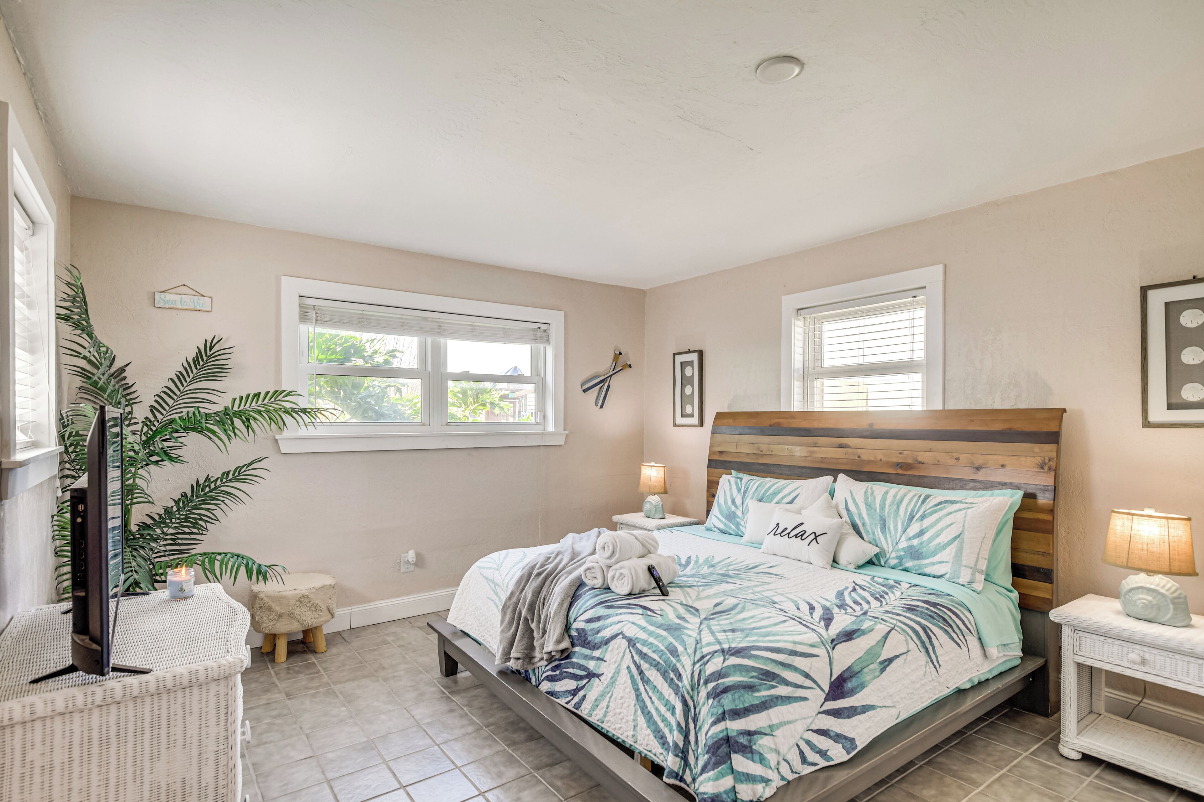 A bedroom with a bed, bedside tables, a lamp, a plant, and a window.