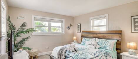 A bedroom with a bed, bedside tables, a lamp, a plant, and a window.