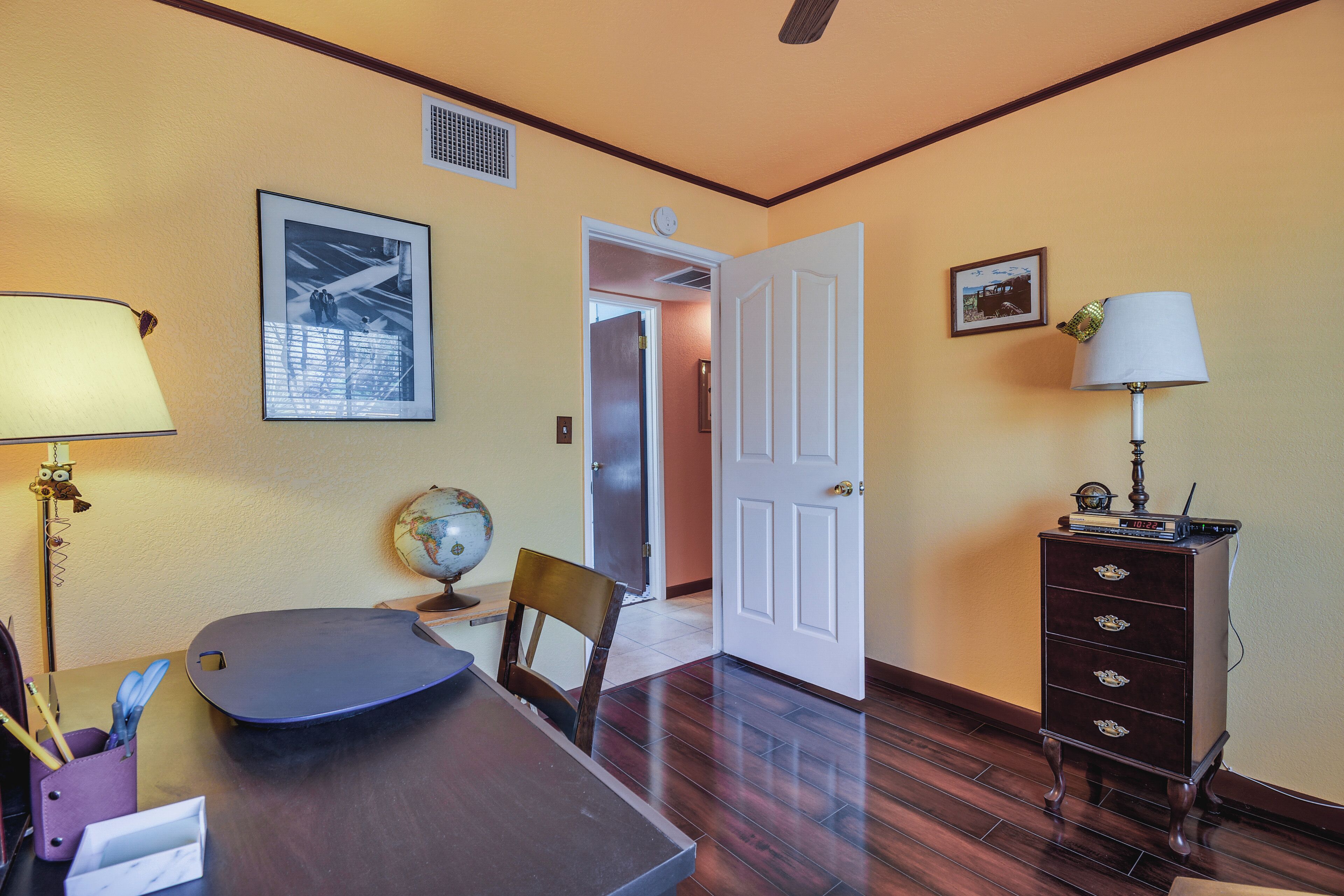 A room with a wooden table, a globe, a framed picture, a lamp, and a dresser.