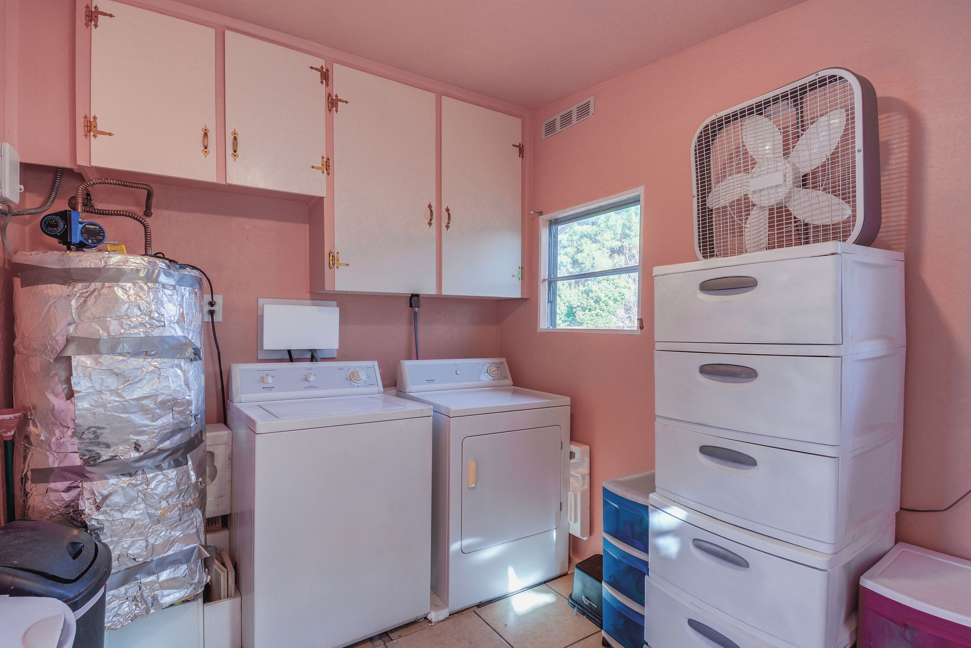 A laundry room with two washing machines, a dryer, a stacked washer, a fan, and a window.
